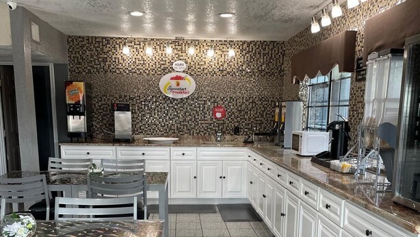 A modern kitchen with white cabinets, a granite countertop, a dining area with a table and chairs, and a backsplash with mosaic tiles.