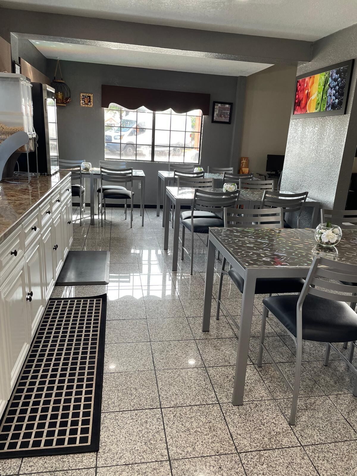 Interior de restaurante con zona de cocina, mesas, sillas y un amplio ventanal.