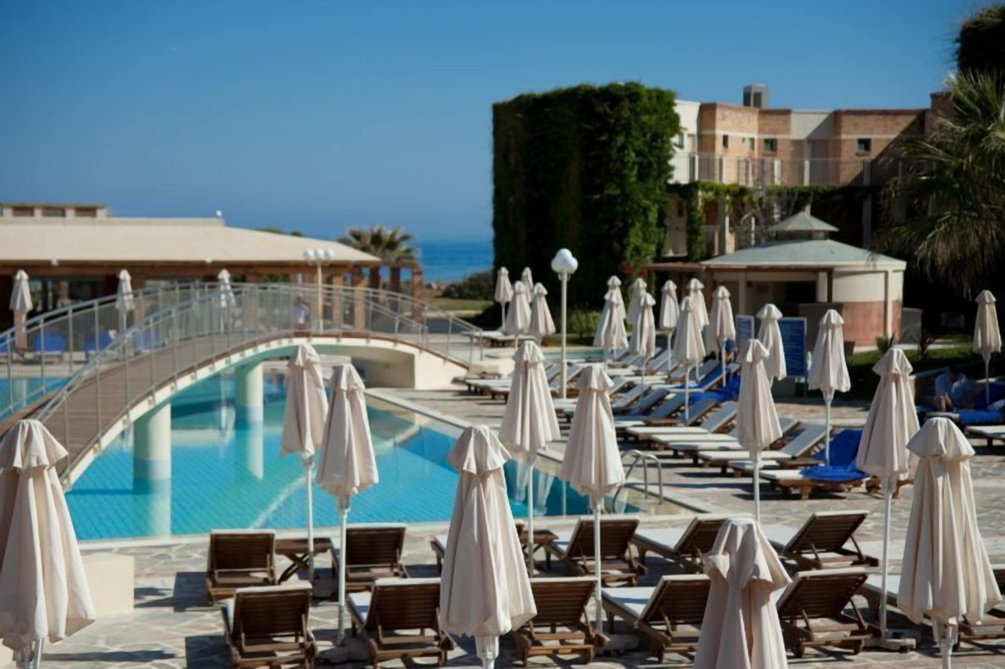 Un espace piscine avec des chaises longues et des parasols, un pont et une vue sur l’océan.