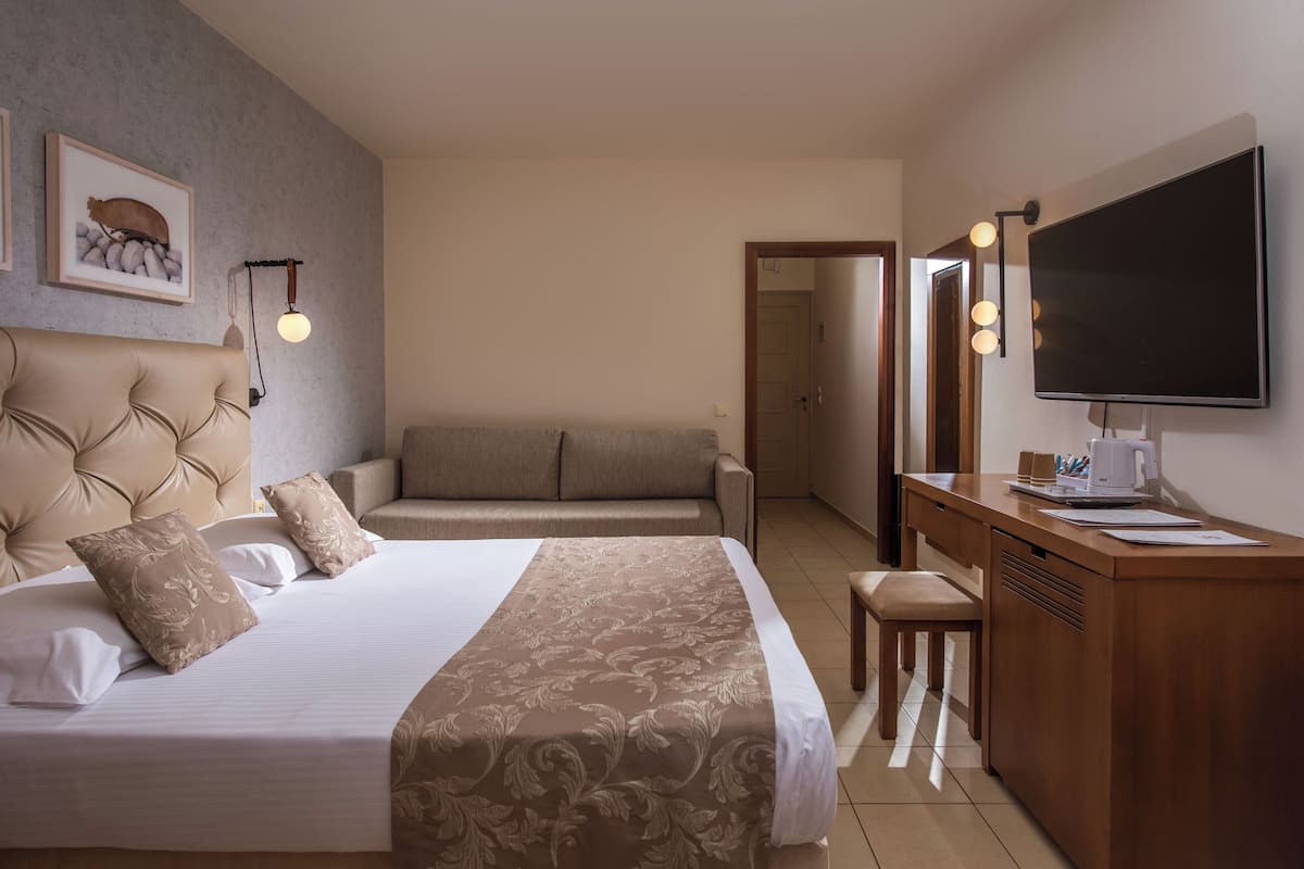 Ein Hotelzimmer mit einem großen Bett, einer Couch, einem Schreibtisch mit einem Flachbildfernseher und einem Spiegel.