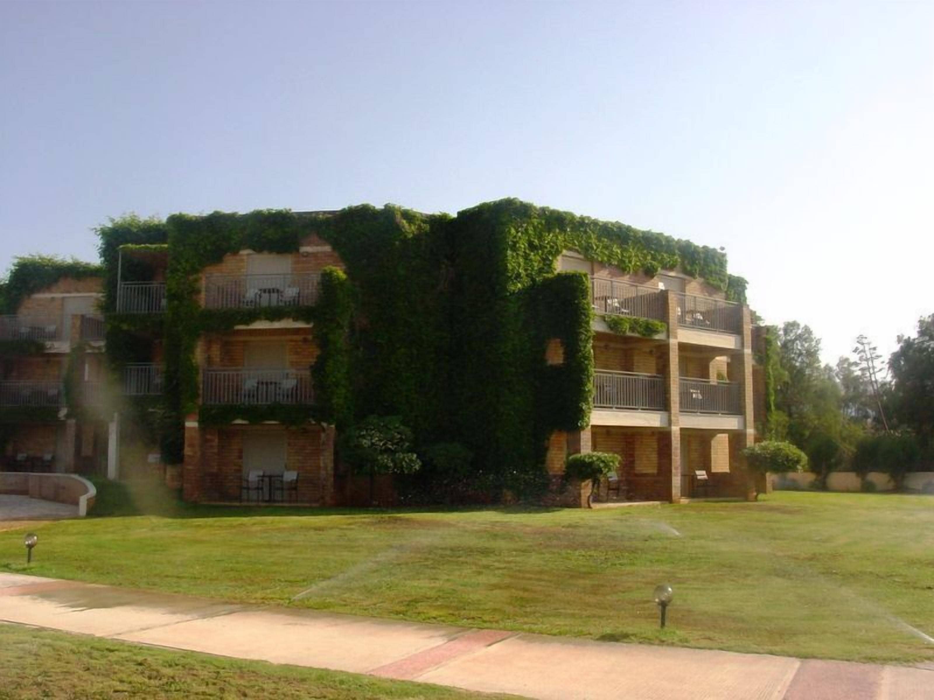 A multi-story building with balconies, surrounded by a well-maintained lawn and a paved walkway.
