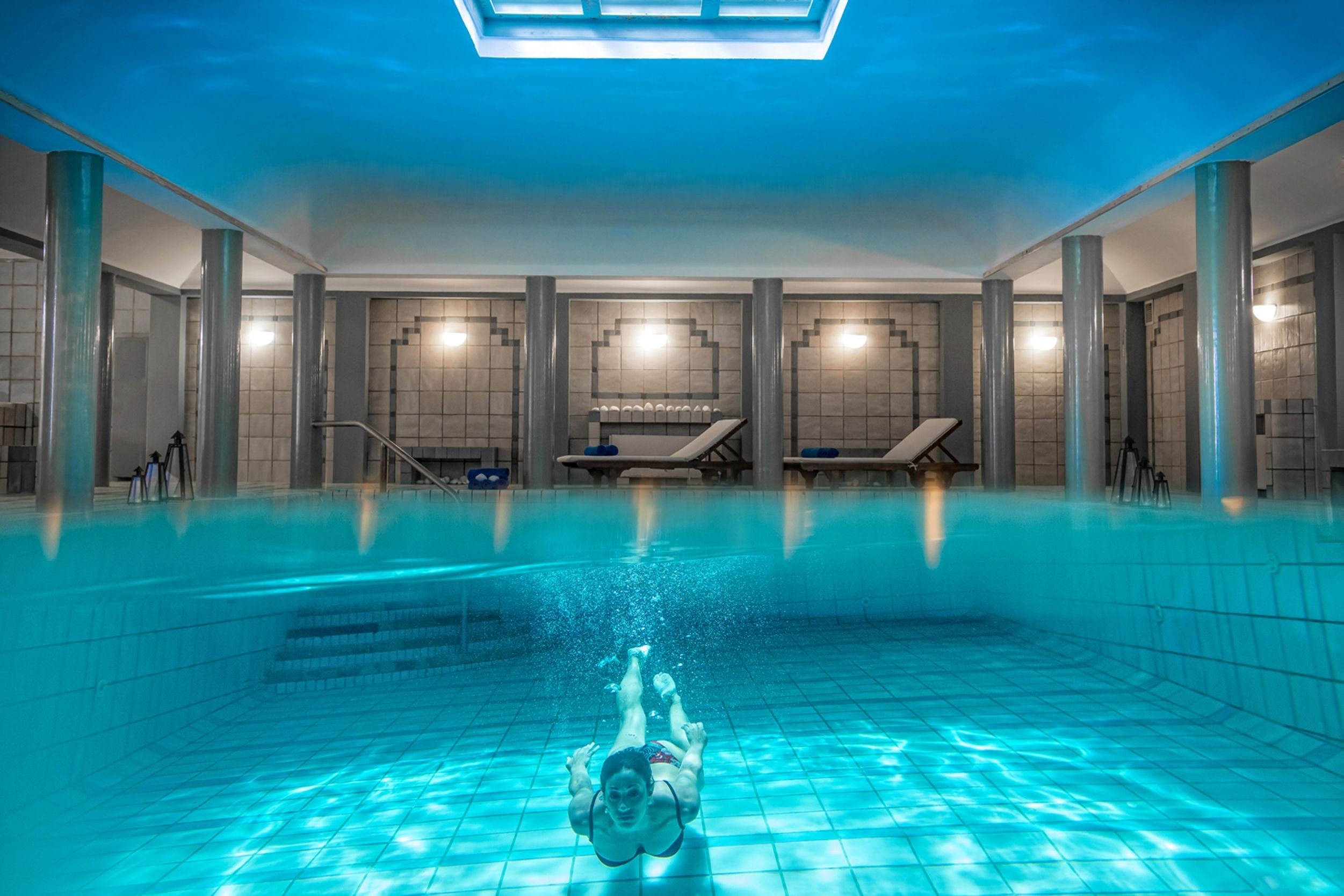 An indoor swimming pool with clear water, tiled walls, and a skylight.