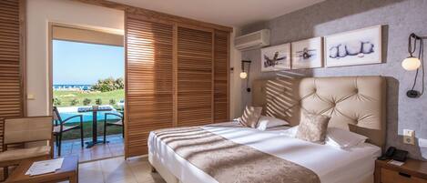 A bedroom with a large bed, a desk, and a view of a pool and greenery.