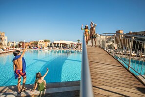 Un área de piscina con terraza de madera, sillas de descanso y sombrillas.