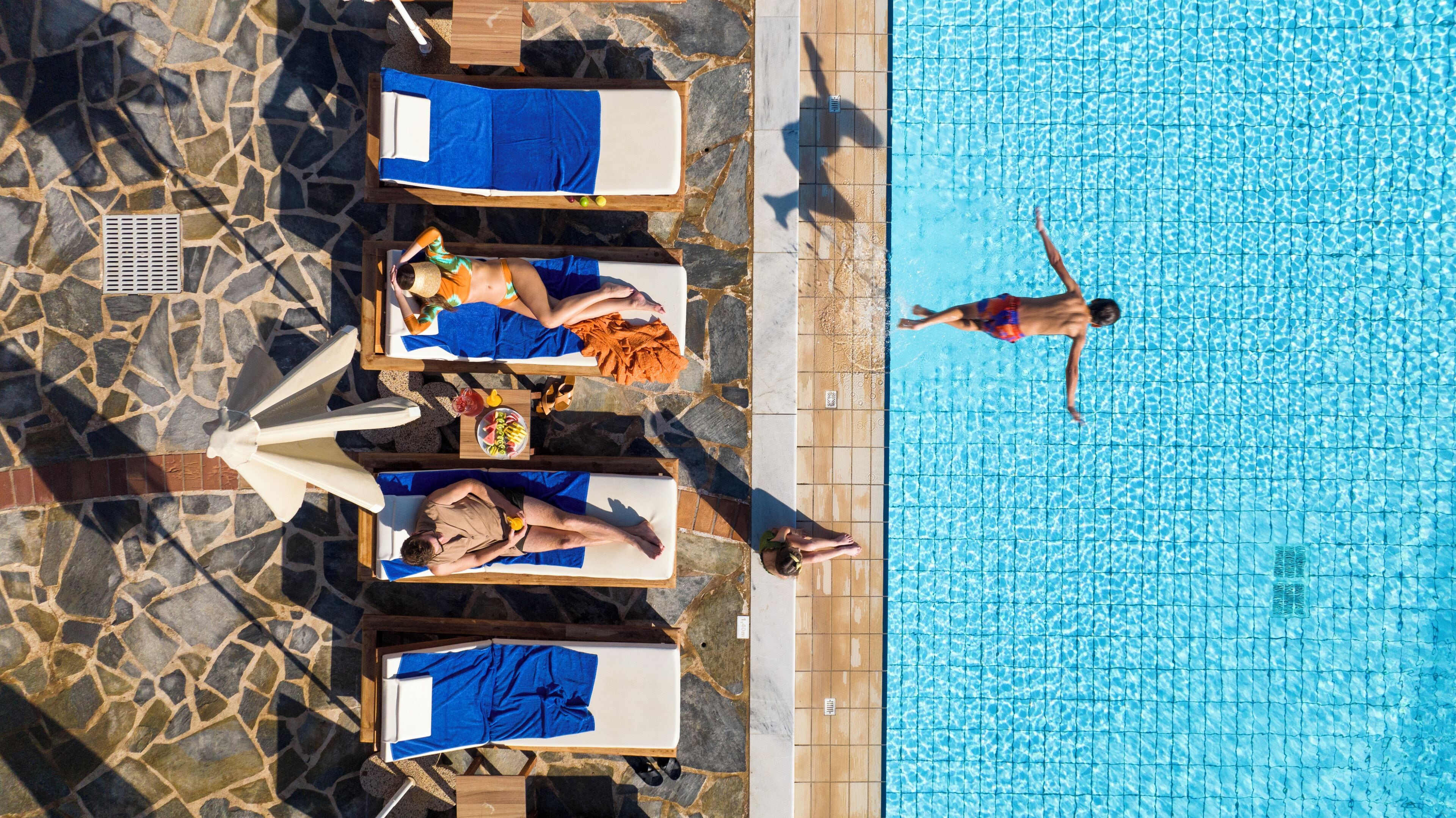 An aerial view of a swimming pool area with lounge chairs and a person swimming.