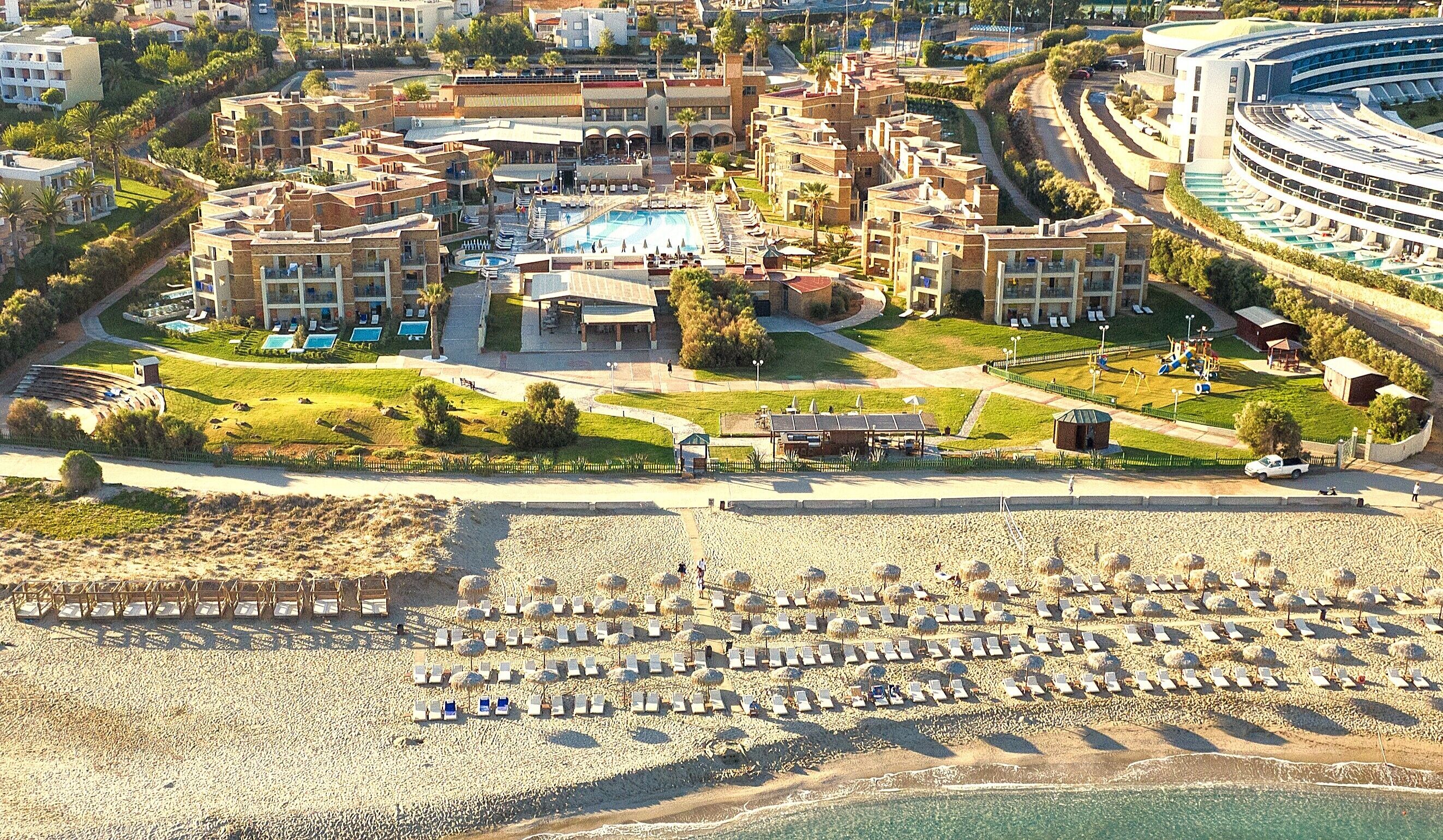 An aerial view of a resort with multiple buildings, a swimming pool, and a beach with sun loungers.