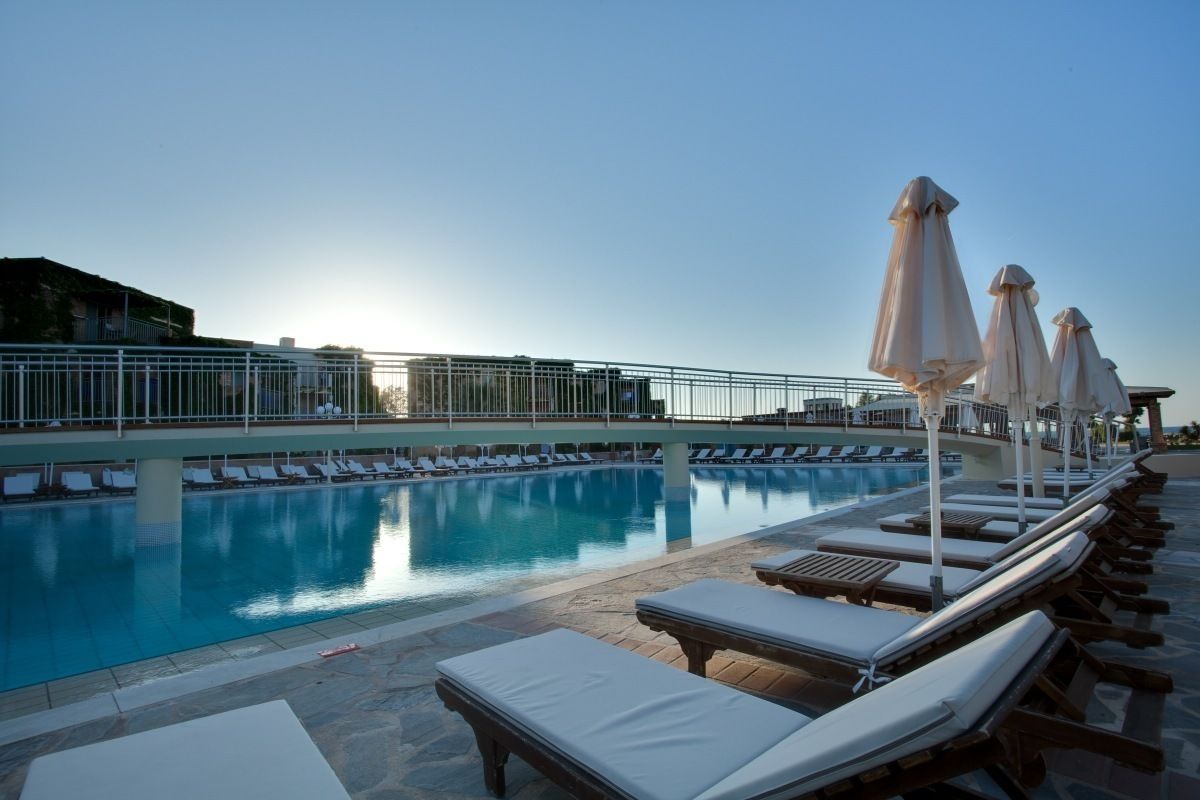 Une piscine entourée d’une clôture et de bâtiments, avec des chaises longues et des parasols.