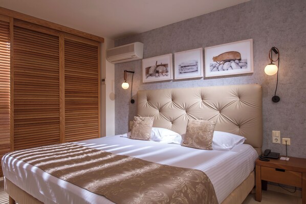 Una cama bien hecha con un cabecero grande, persianas de madera a la izquierda y dos lámparas fijadas a la pared.