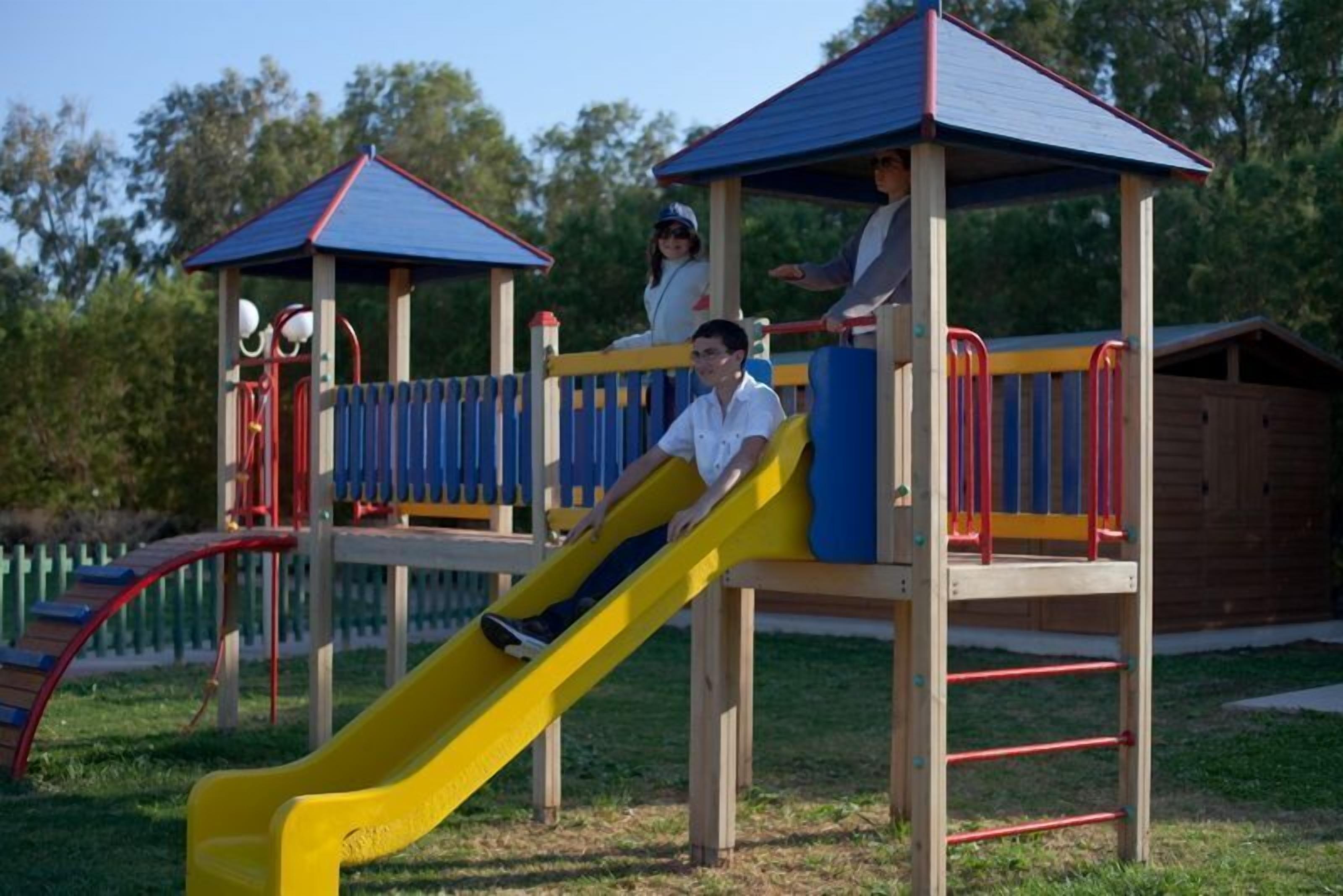 A playground with a yellow slide, wooden play structures, and covered seating areas.