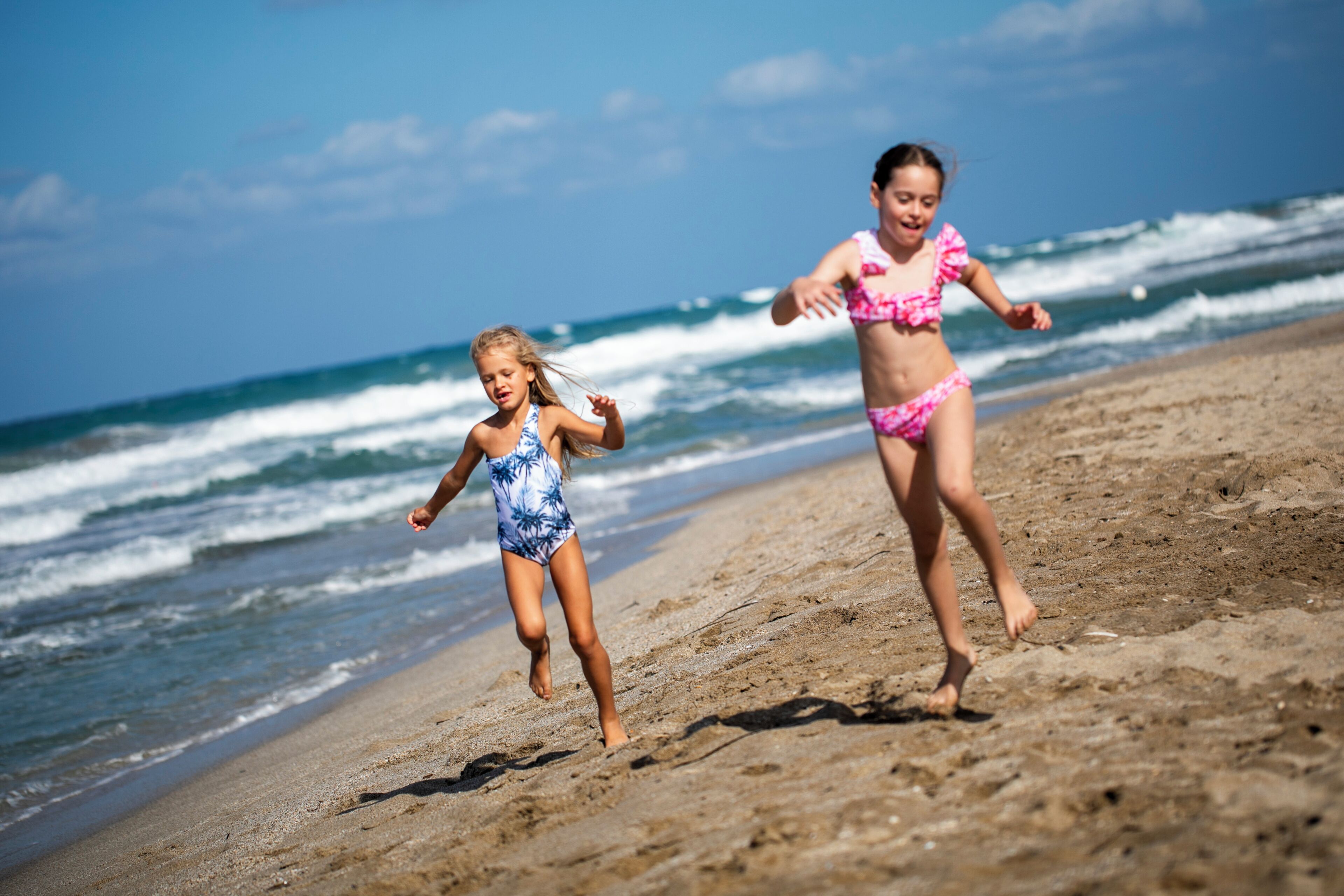 Twee kinderen rennen over een zandstrand, met golven op de achtergrond.