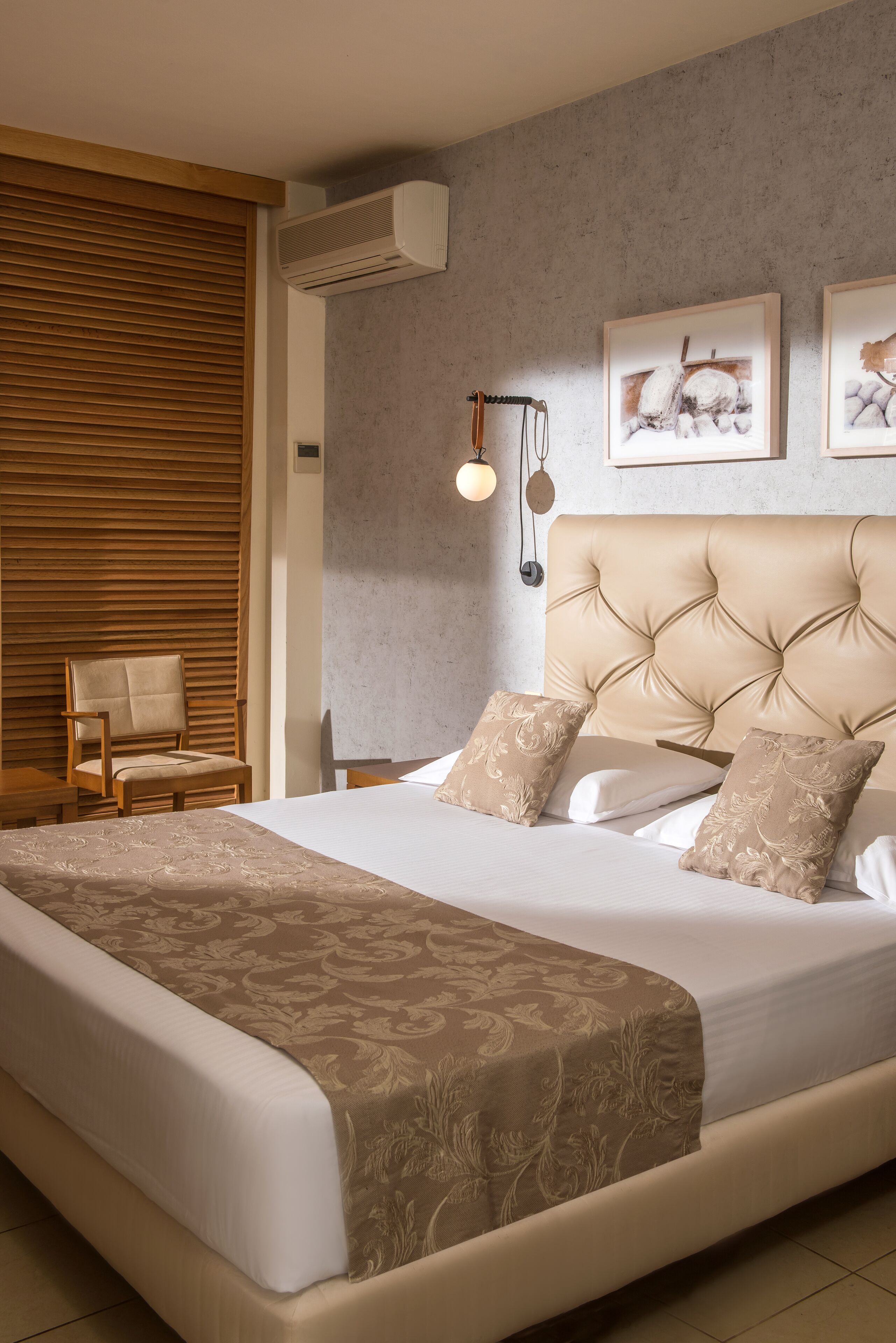 Egy hálószoba, amelyben egy nagy ágy, egy fa szék, egy a falra szerelt légkondicionáló és keretezett képek találhatók a falon.