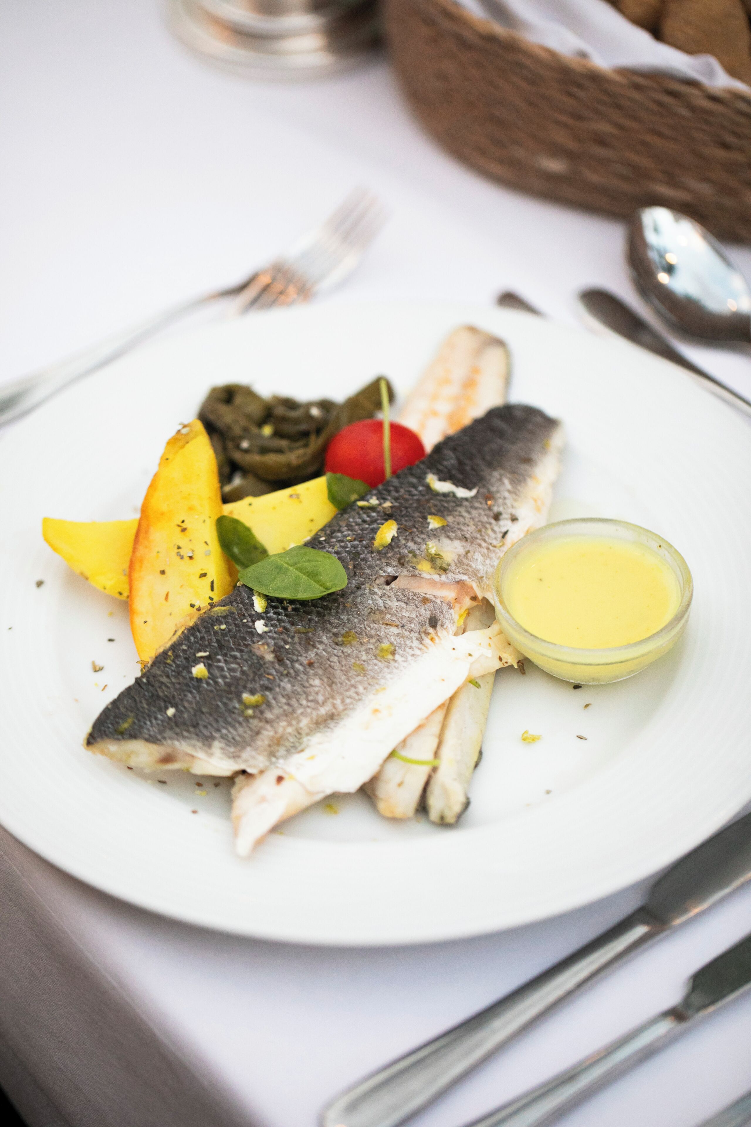 Un plato con pescado, verduras y un recipiente pequeño de salsa.