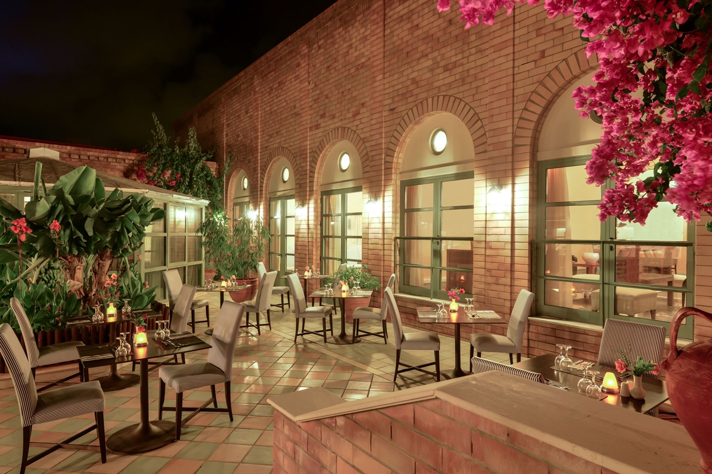 An outdoor patio with brick walls, arched windows, and tables with chairs.