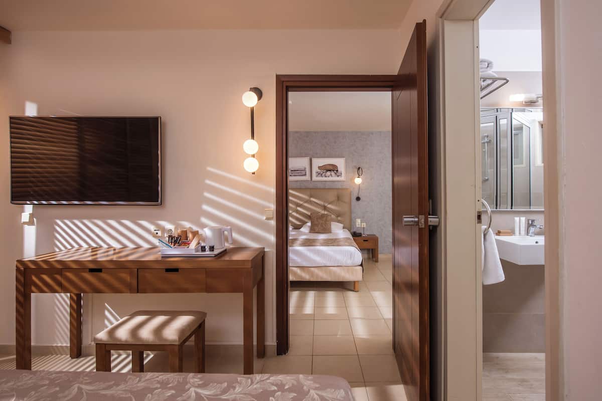 Ein Hotelzimmer mit einem Holztisch, einem Bett, einem Spiegel und einem durchgegangene Tür erkennbaren Badezimmer.