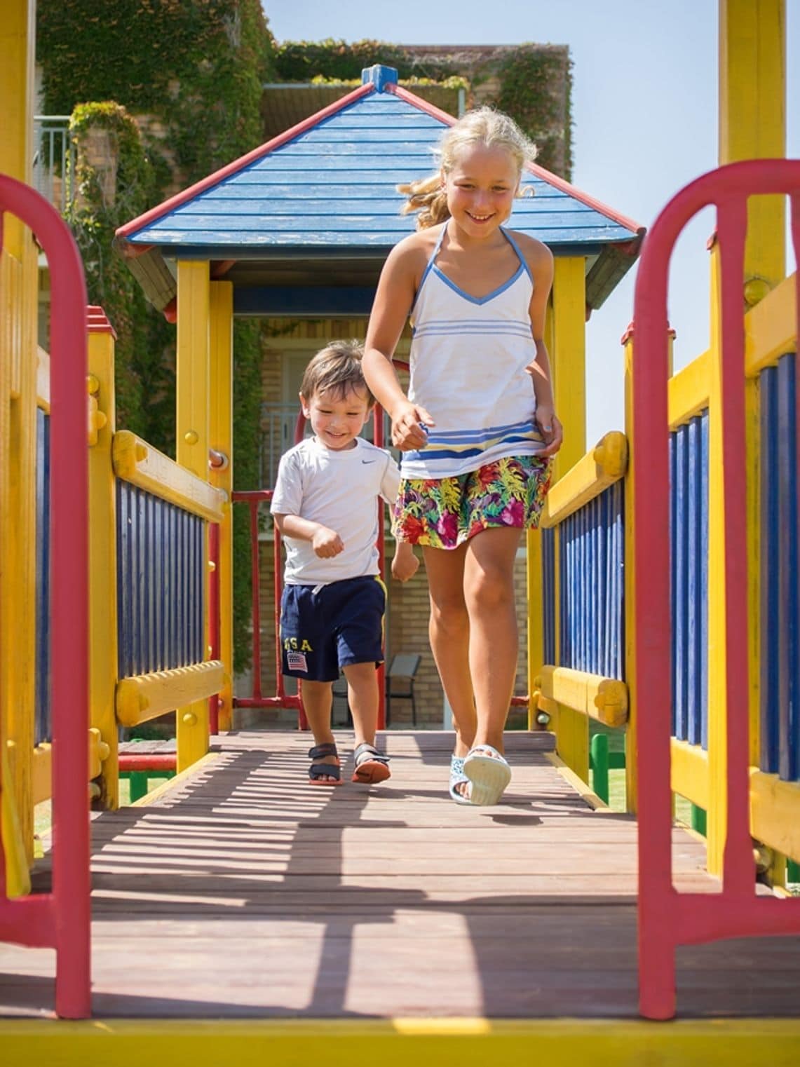 A wooden pedestrian bridge with yellow and red railings, leading to a blue-roofed structure.