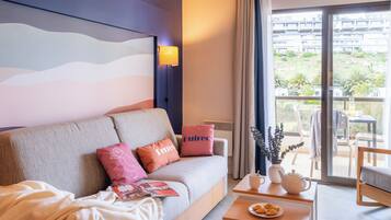 Een moderne hotelkamer met een bank, kussens, een tafel met een theepot en uitzicht op het balkon.