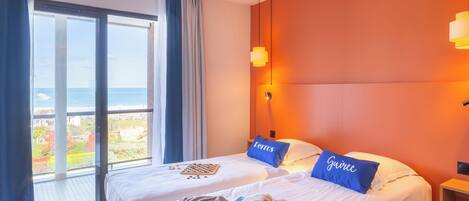Ein Hotelzimmer mit großem Fenster, einem Bett mit zwei Kissen, einem Nachttisch und Blick auf das Meer.