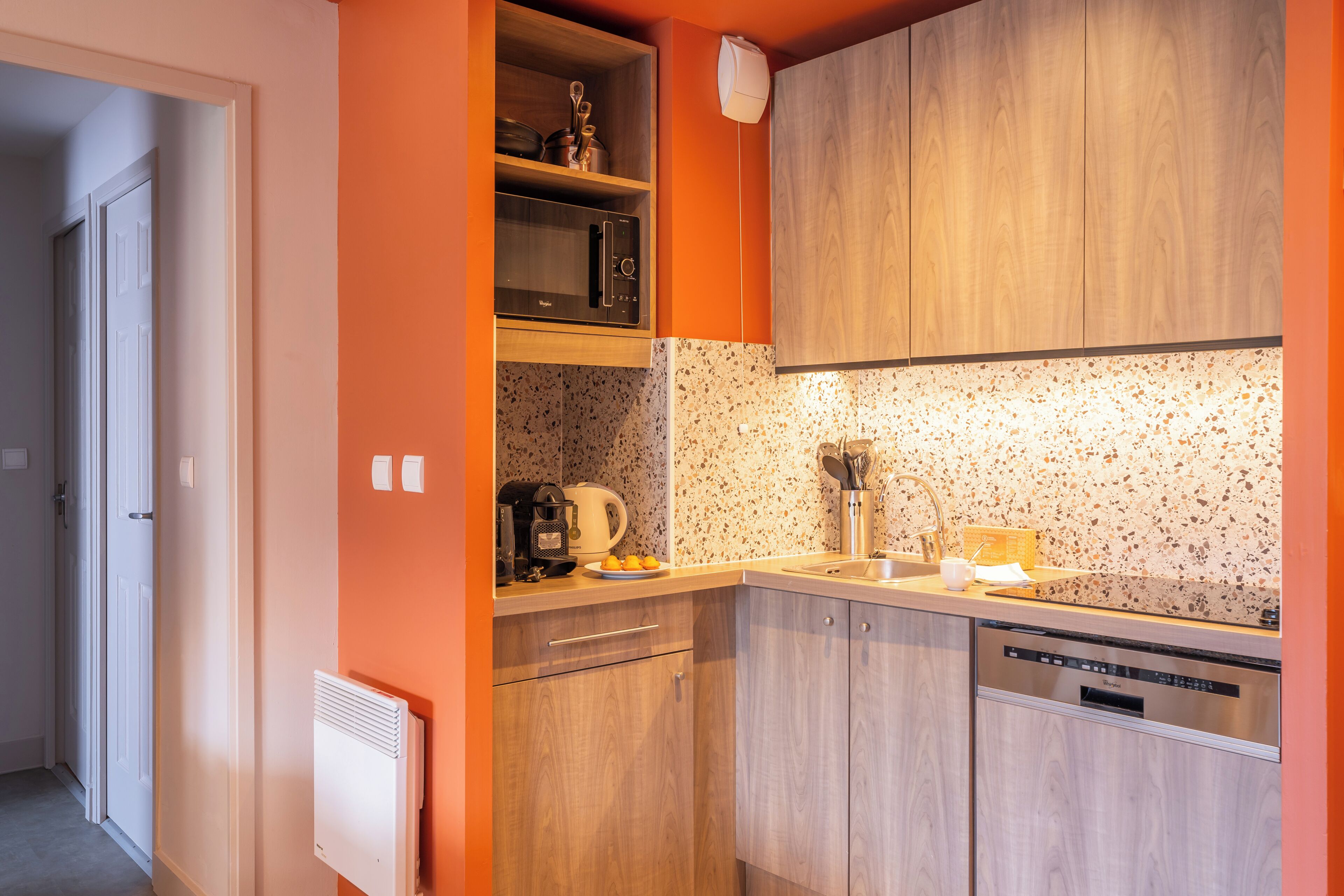A compact kitchen with wooden cabinets, a microwave, a coffee maker, and a dishwasher.