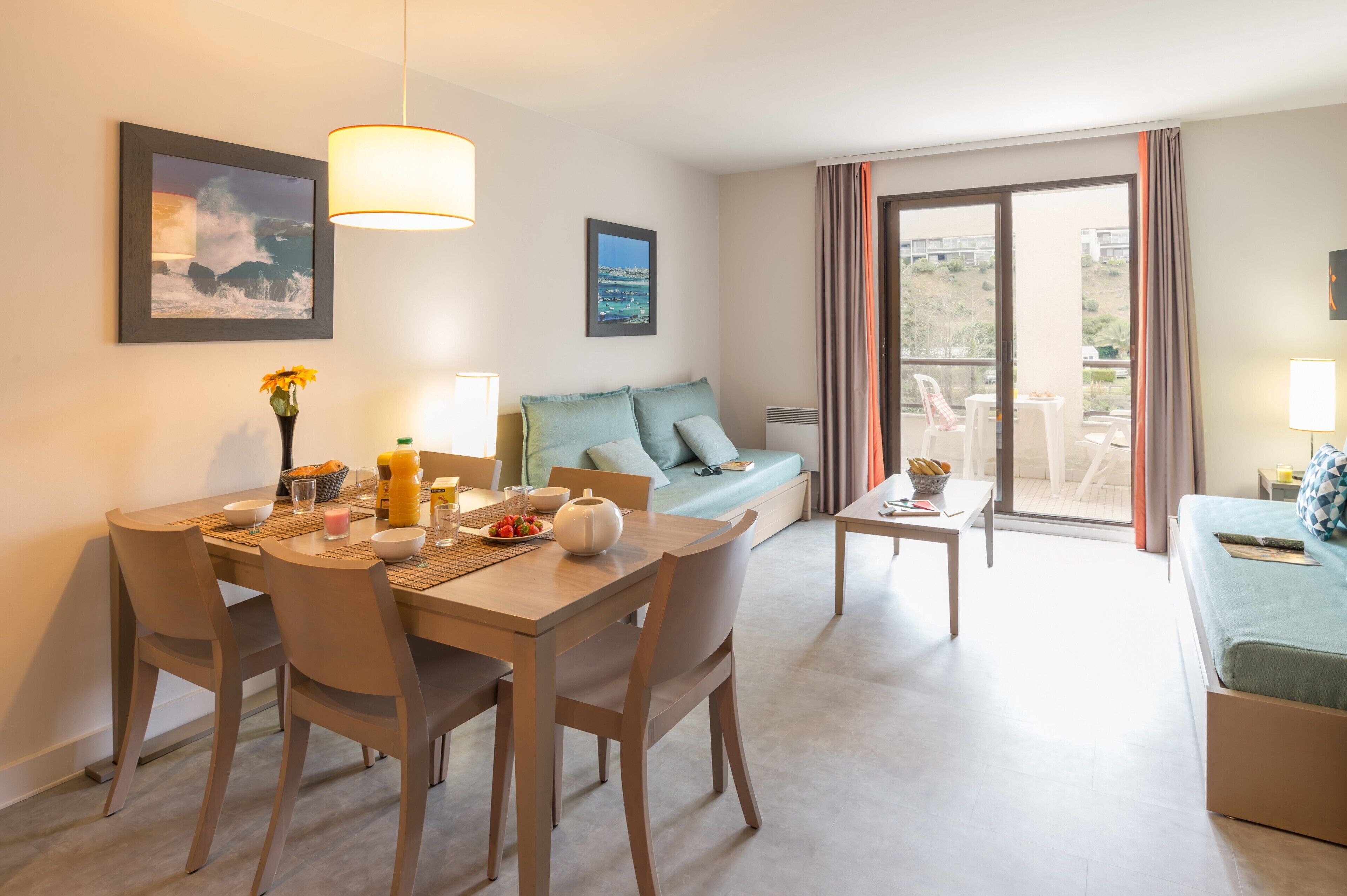 A modern hotel room with a dining area, a sofa, and a balcony with a view.