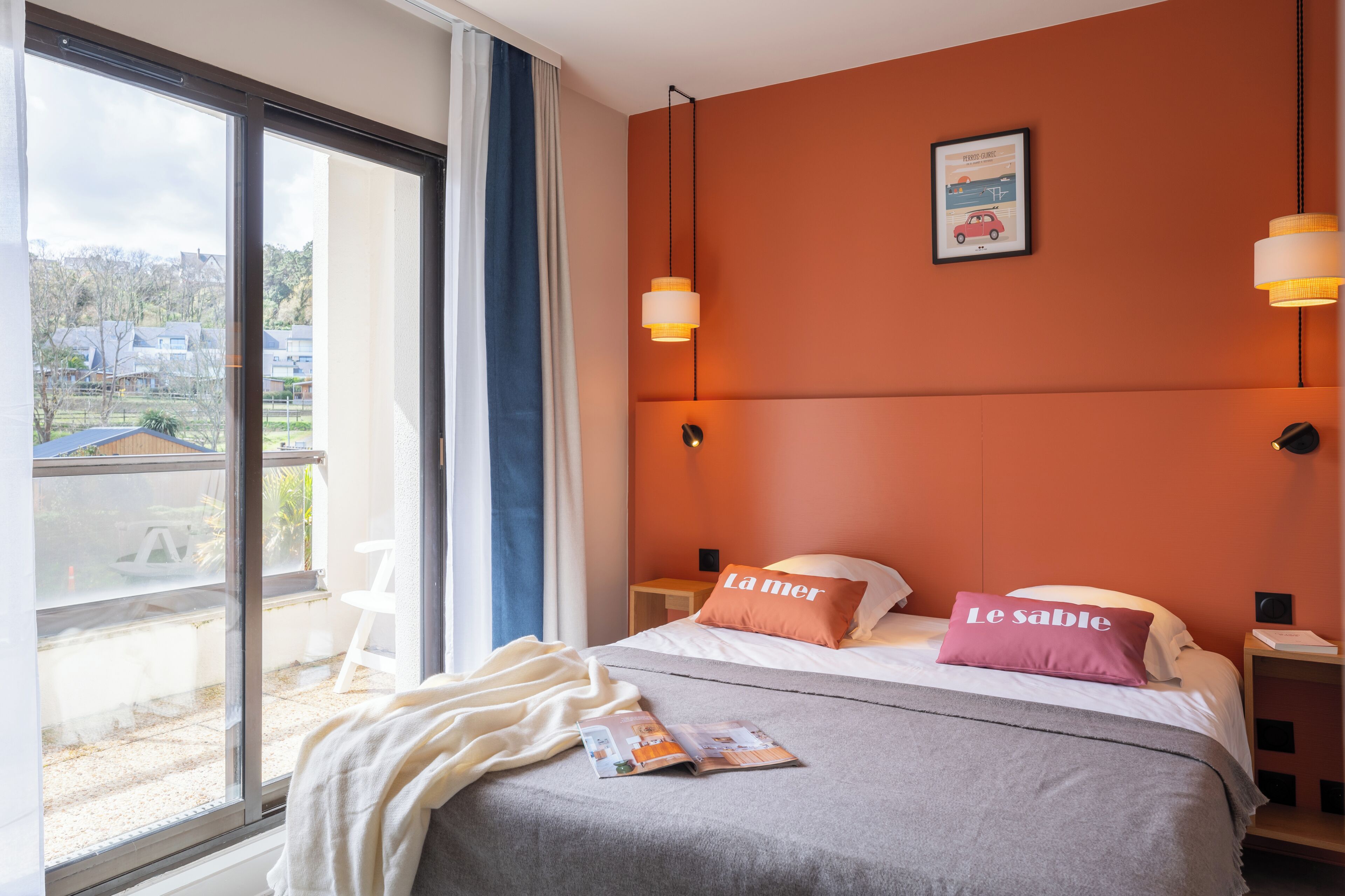 A bedroom with a large window, a bed with two pillows, a bedside table, and a view of the outside.