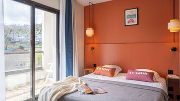 A bedroom with a large window, a bed with two pillows, a bedside table, and a view of the outside.