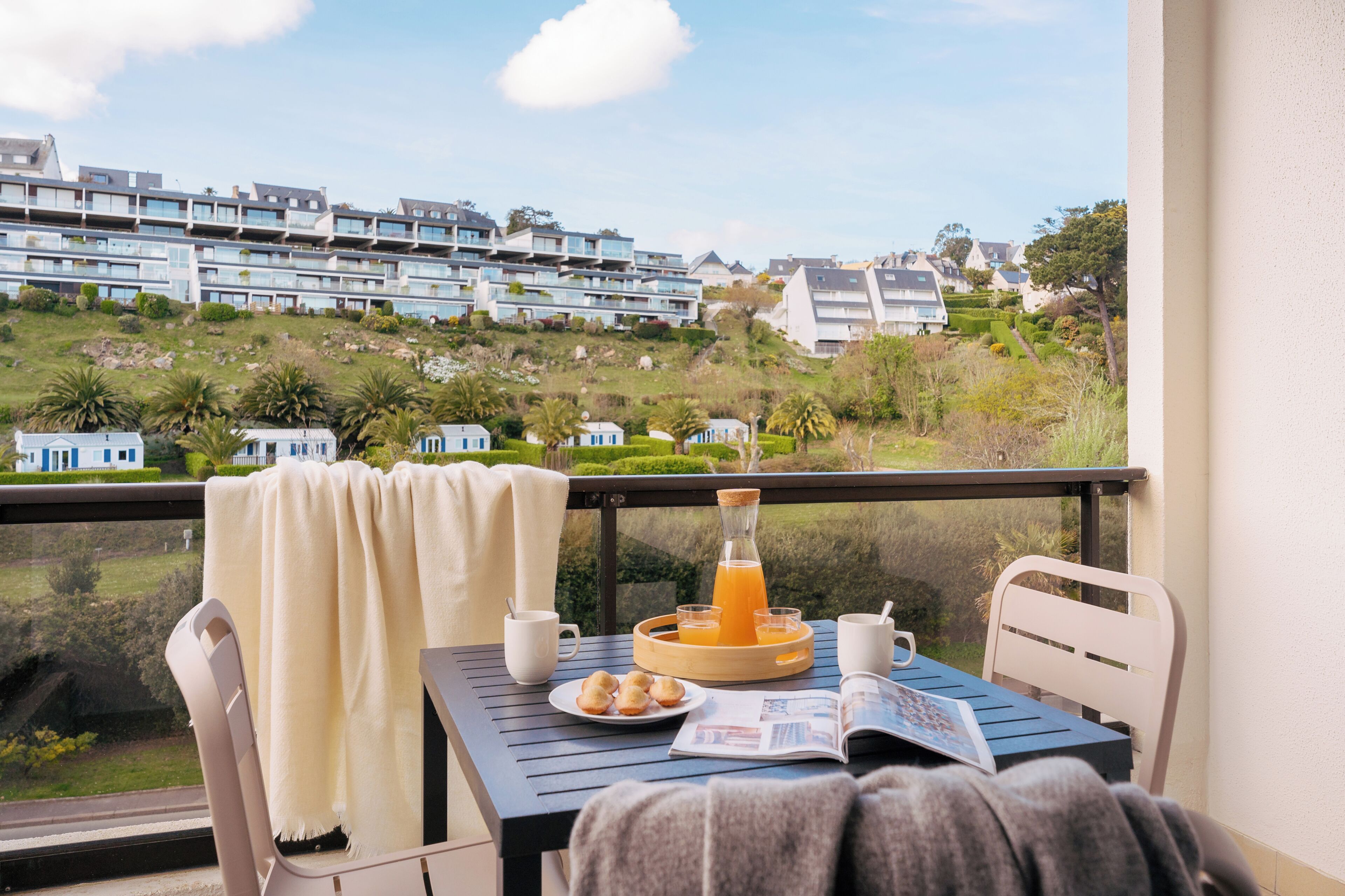 A balcony with a table set for breakfast, a view of residential buildings, and a clear sky.
