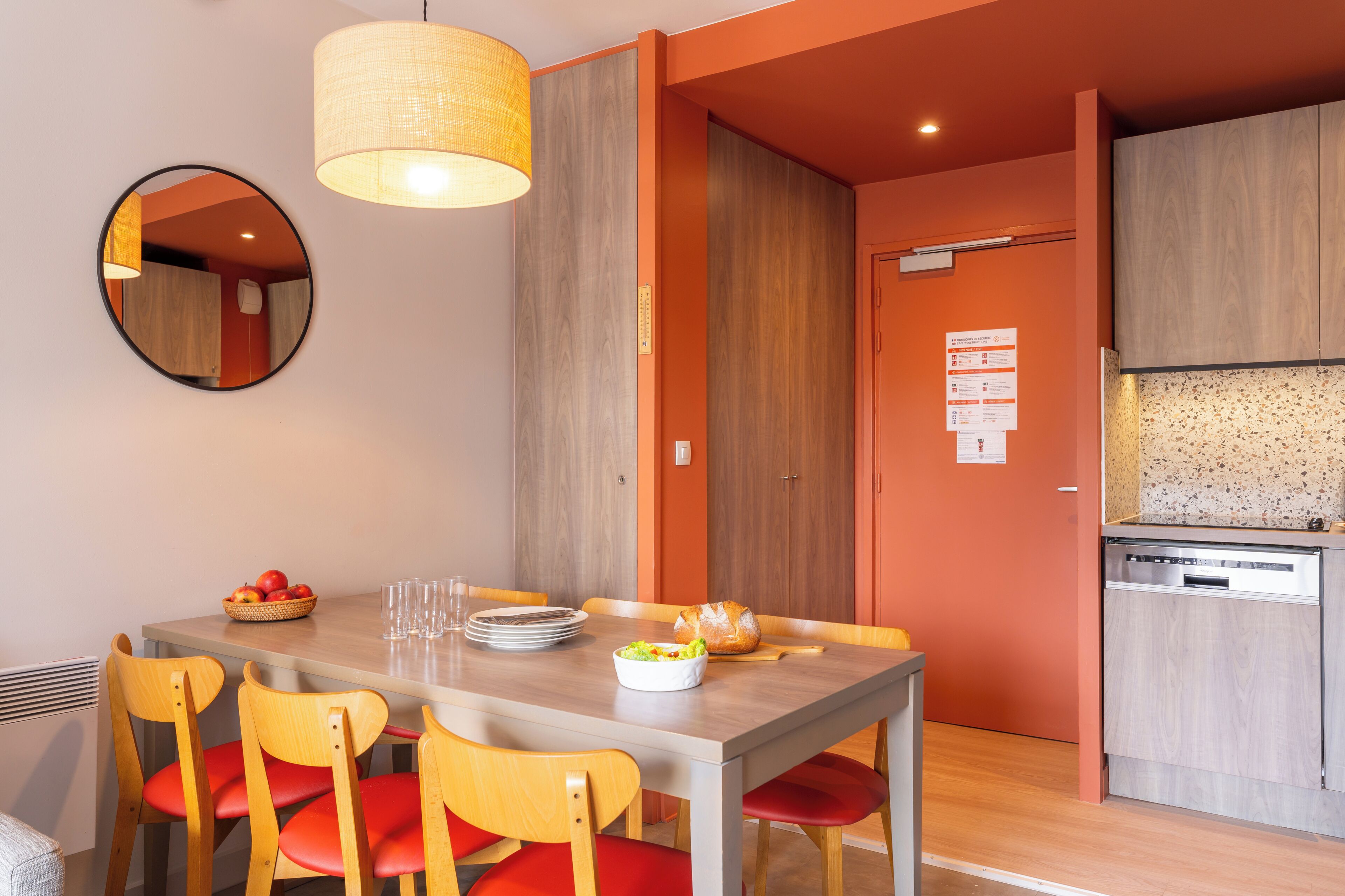 A modern kitchen with wooden cabinets, a built-in dishwasher, and a dining area with a wooden table and red chairs.
