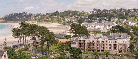 A coastal town with a prominent hotel featuring multiple floors, a beach, and lush greenery.