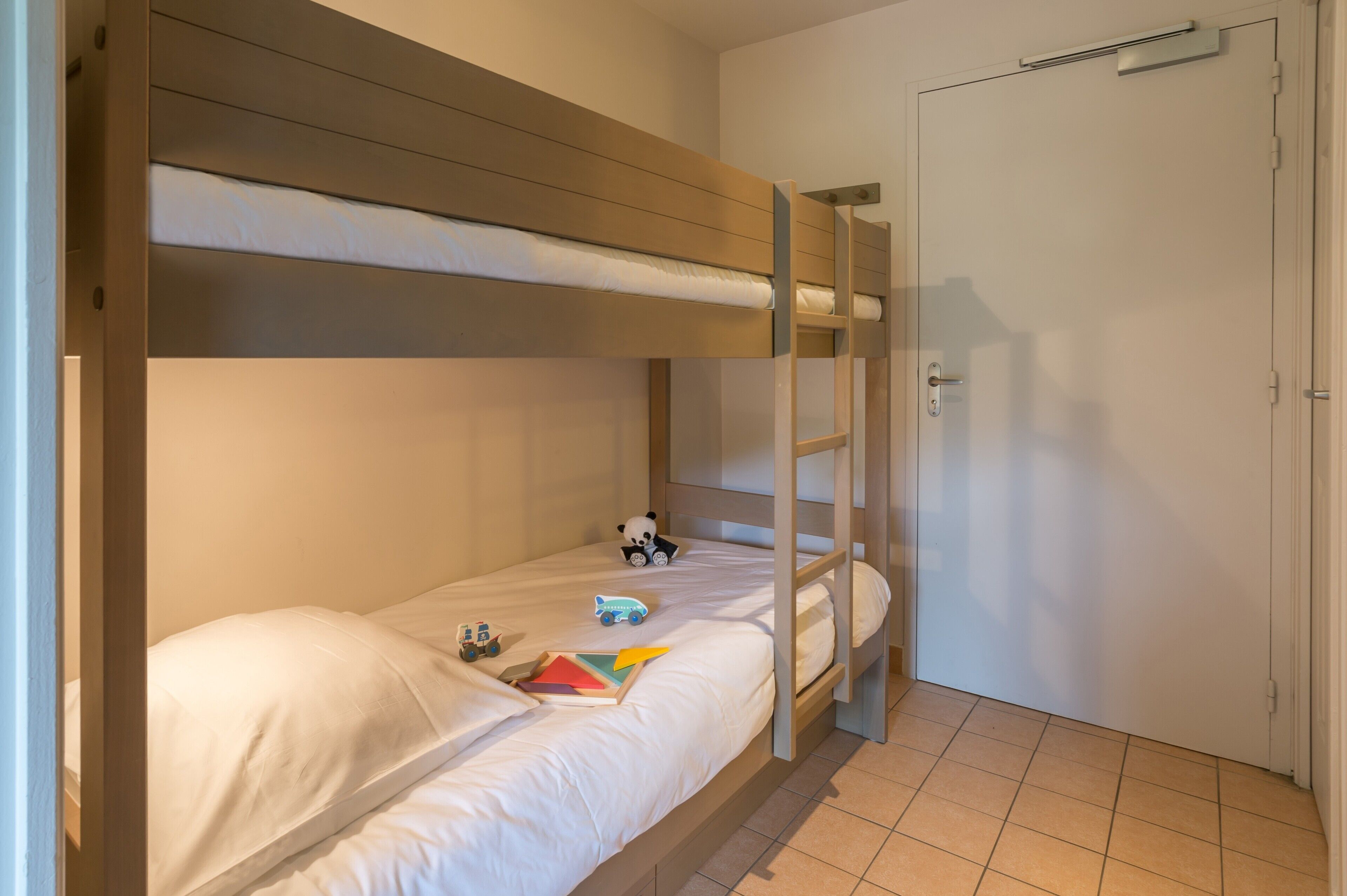 A bunk bed with a wooden headboard, a white door, and a tiled floor.