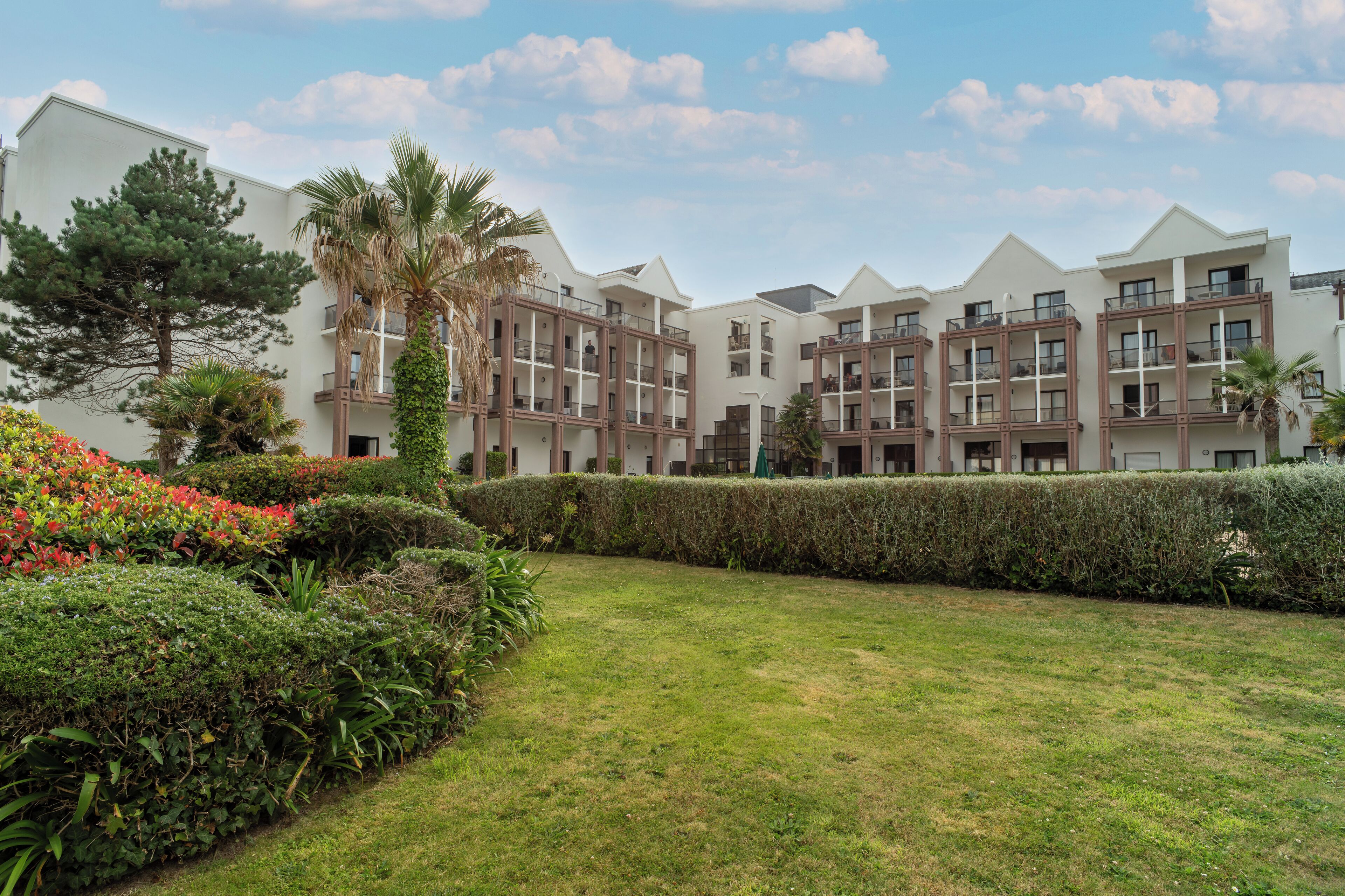 A multi-story residential building with balconies, surrounded by well-maintained hedges and a grassy lawn.