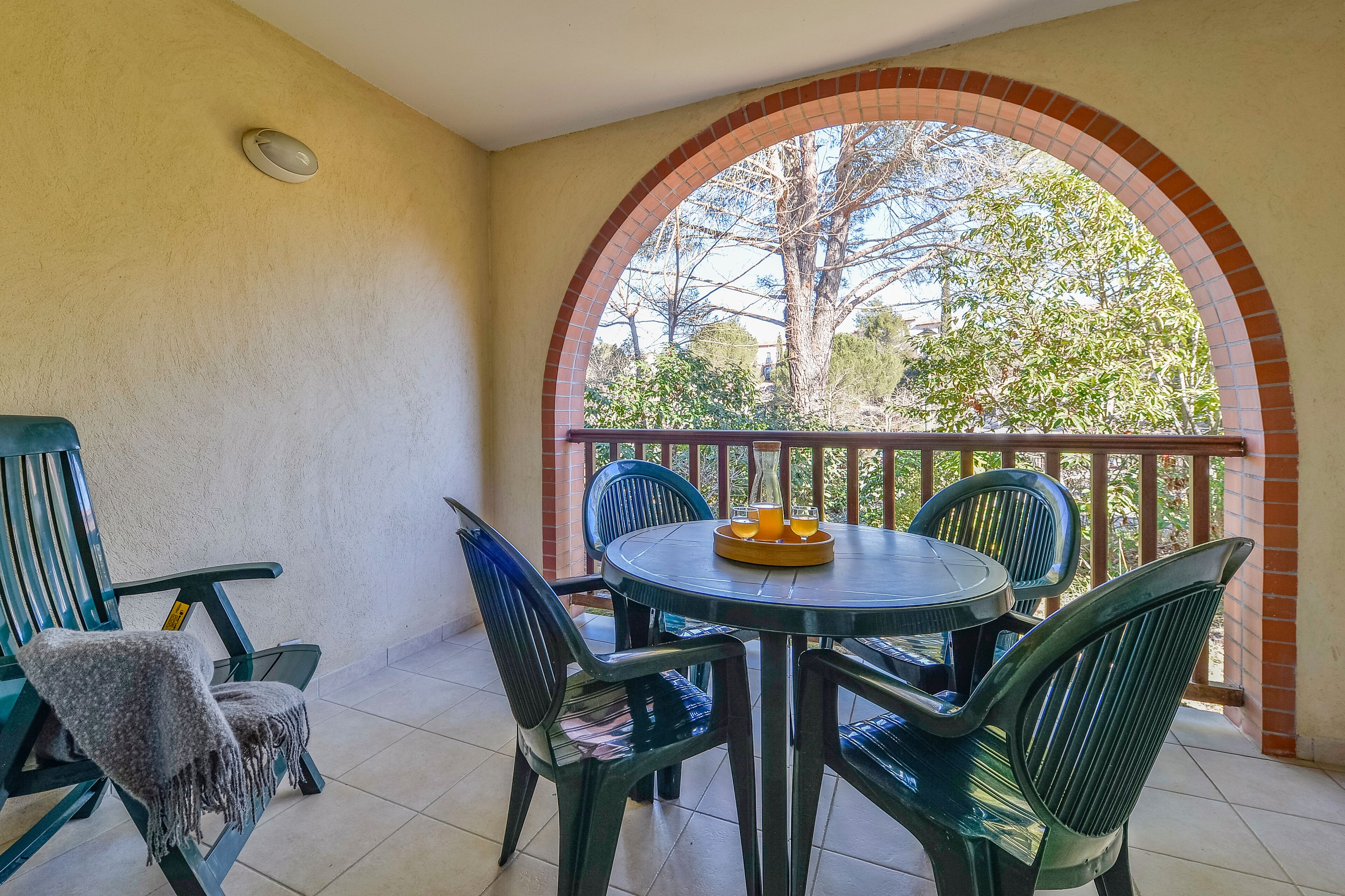 A balcony with a round table and chairs, a small covered seating area, and a view through an arched window.