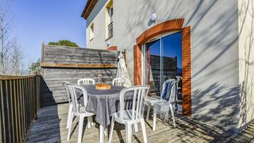 Relax in a comfortable outdoor space with a round table and chairs, surrounded by a wooden deck and brick-stucco walls.