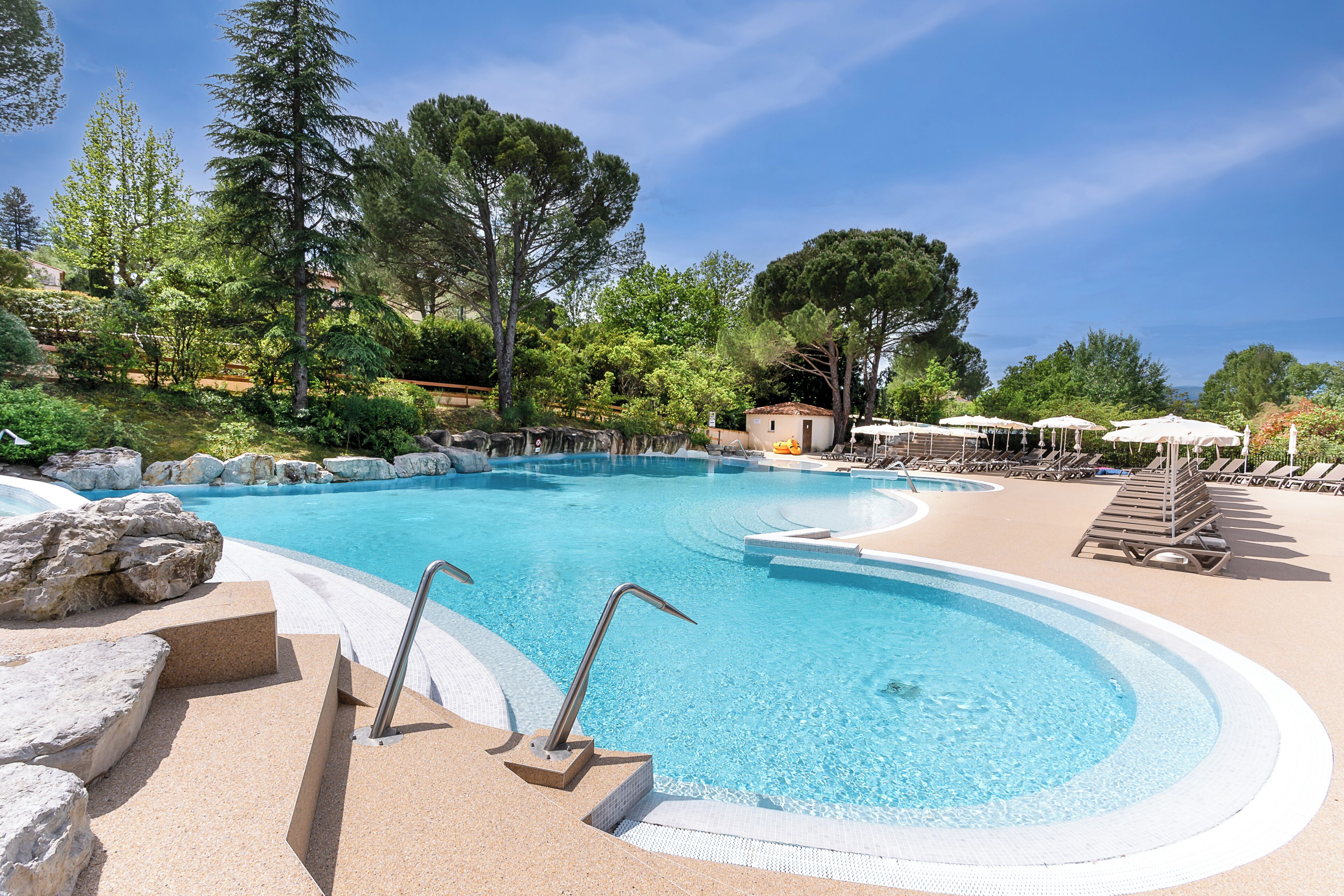 A swimming pool with steps leading into it, surrounded by lounge chairs and umbrellas.