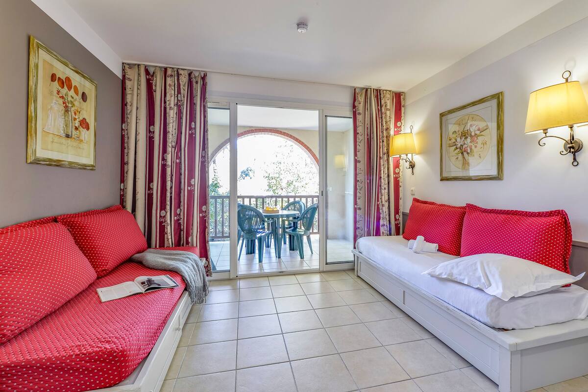 Une chambre d’hôtel avec un canapé rouge, un lit blanc et un balcon équipé d’une table et de chaises.