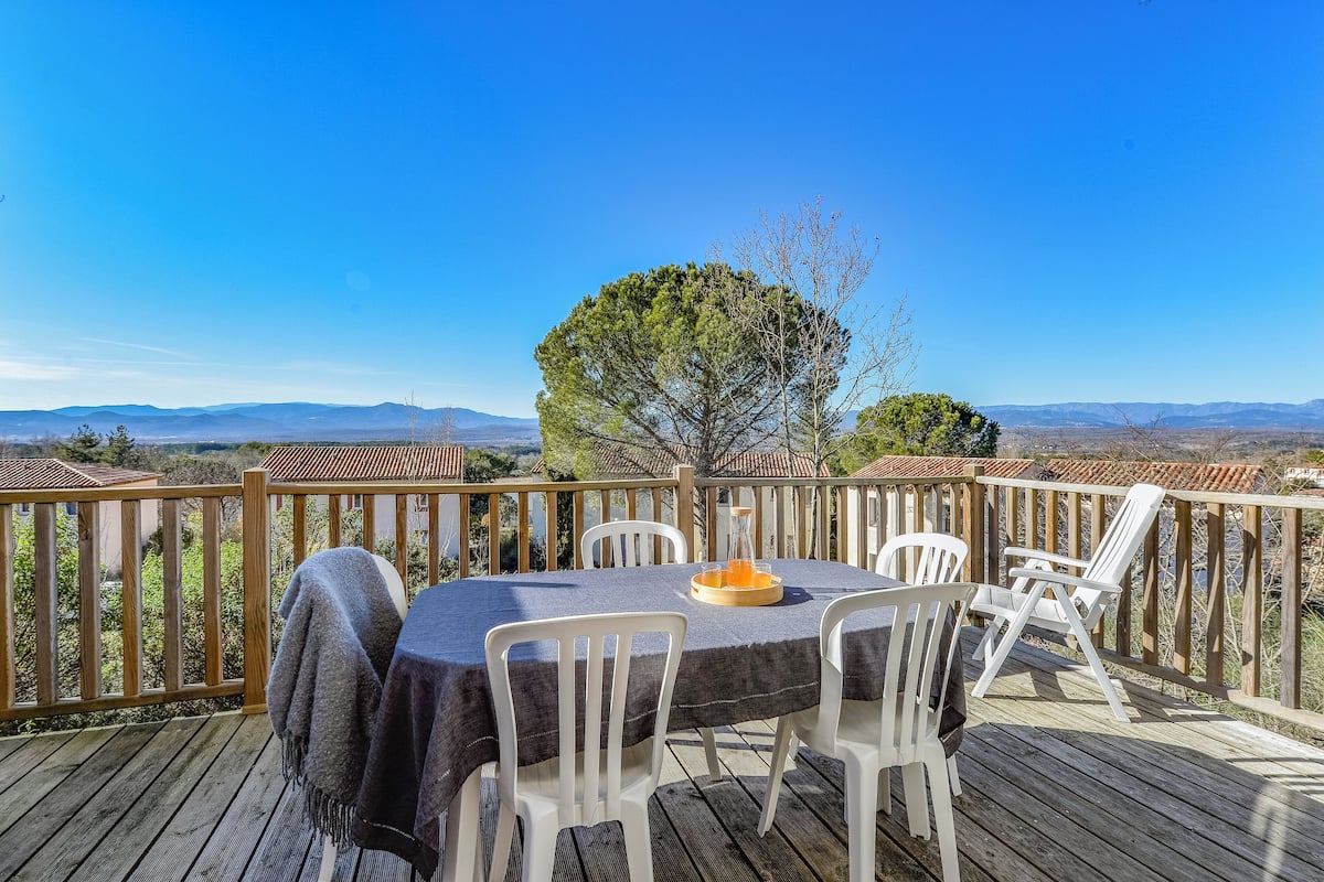 Une terrasse en bois avec une table et des chaises, offrant une vue sur un paysage magnifique.