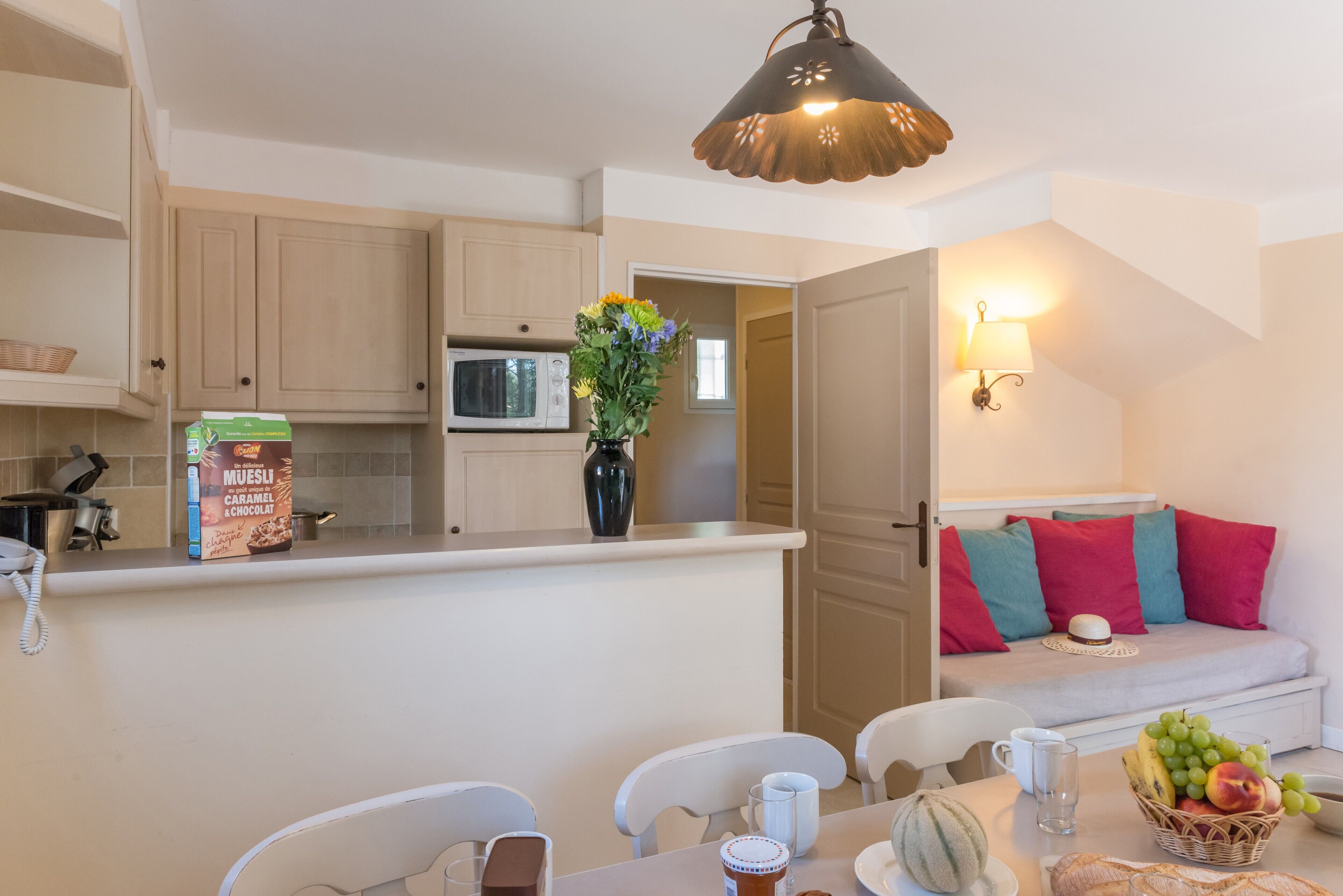 A compact kitchen with a microwave, a vase with flowers, and a box of Muesli on the counter.