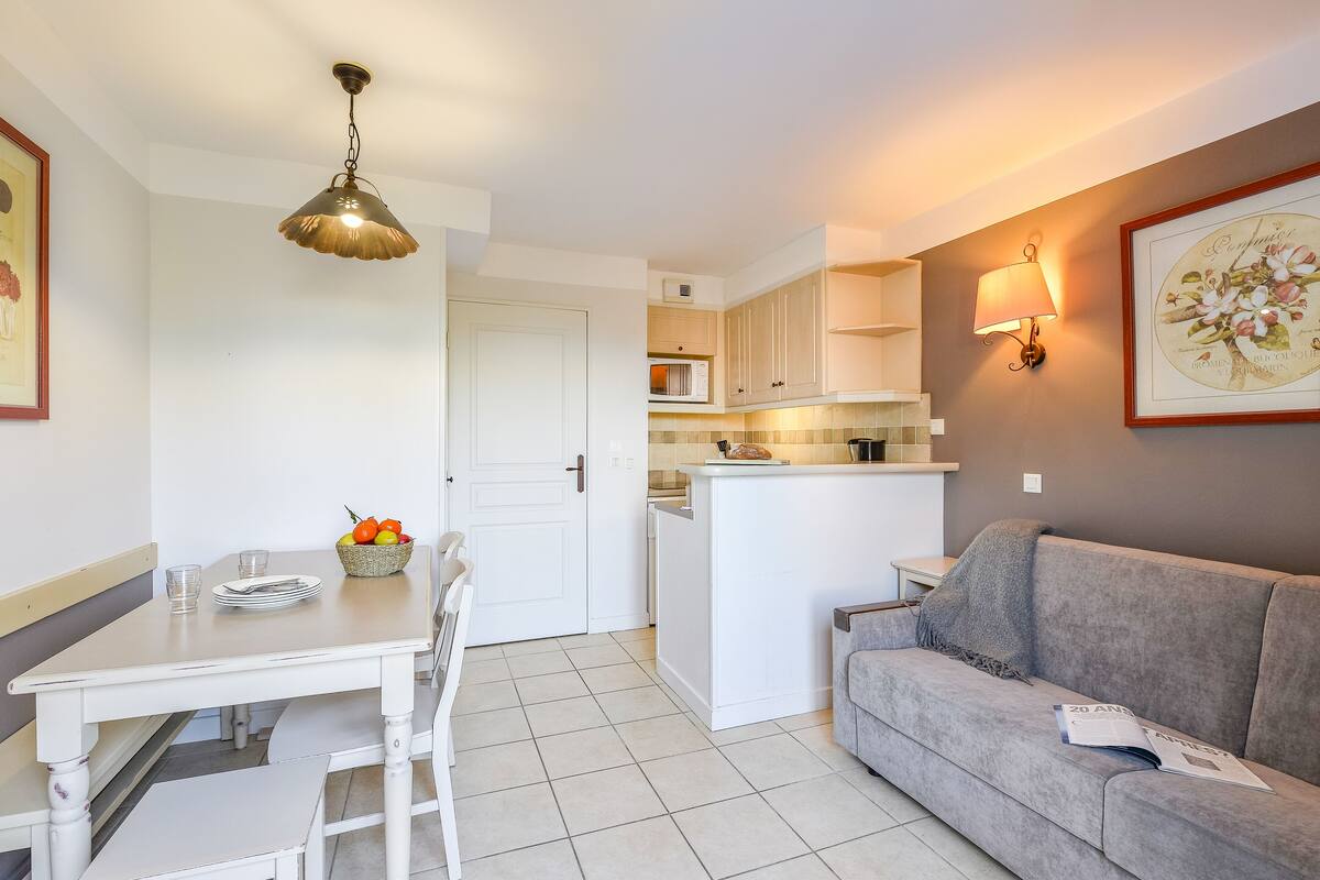 Une cuisine de taille réduite avec une table à manger, un canapé gris et une lampe fixée au mur.