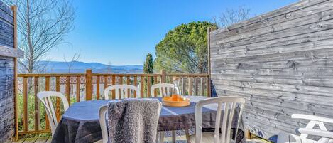 An outdoor patio with a table set for two, surrounded by white chairs, overlooking a scenic view of mountains and trees.