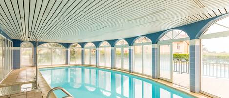 An indoor swimming pool with clear glass walls, a tiled floor, and a ceiling with wooden slats.