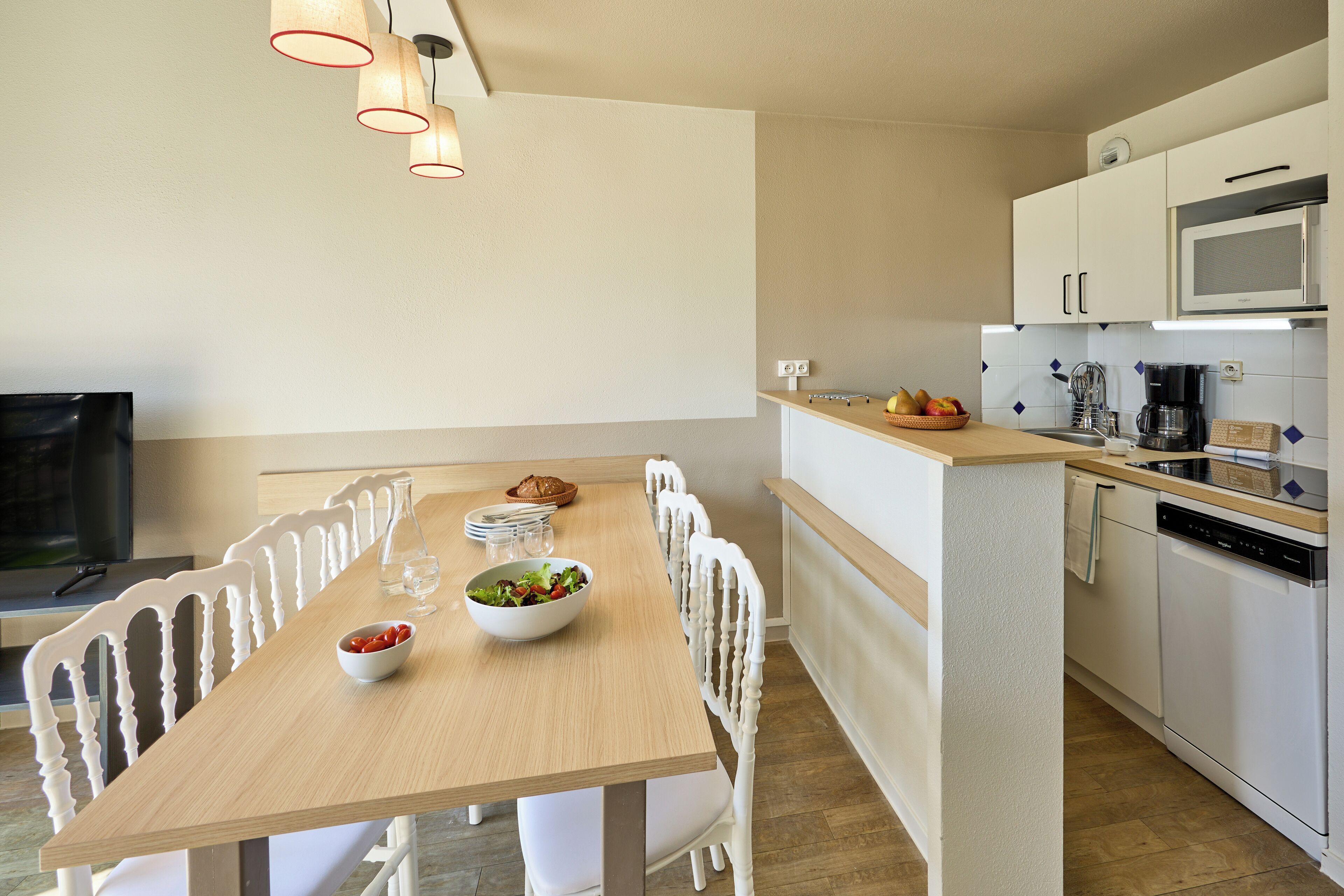Een moderne keuken met witte kastjes, een houten eettafel en een inbouwmagnetron.