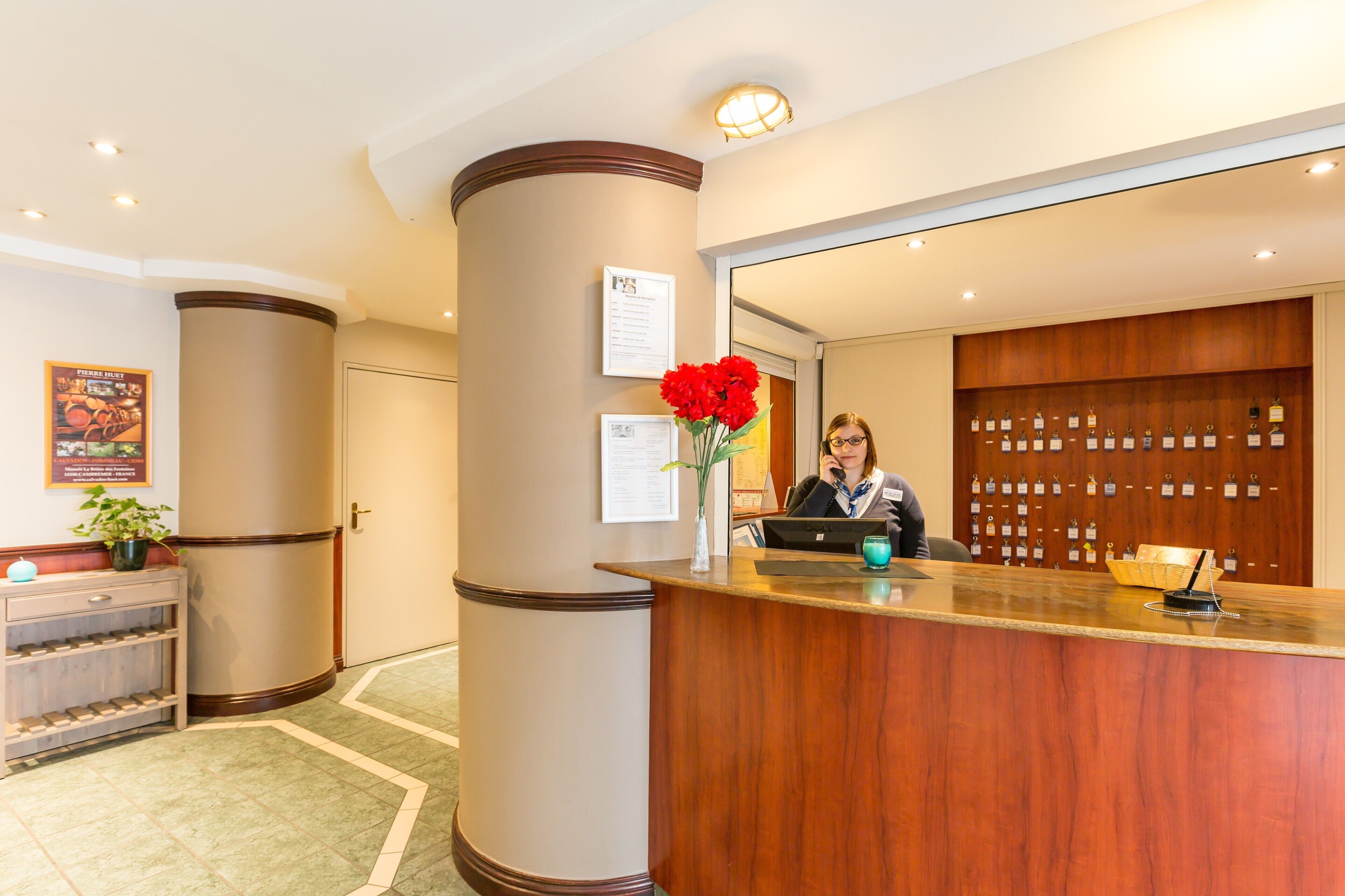 Zona de recepción de un hotel con un mostrador de madera, una planta en maceta y un panel con llaves de las habitaciones.