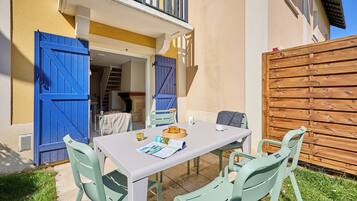 Een terras met een tafel en stoelen, een houten hek en een gebouw met blauwe luiken.