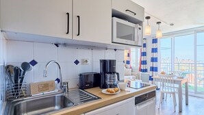 A modern kitchen with a dishwasher, a coffee maker, and a microwave. There is a window with curtains and a view of buildings outside. - Pierre & Vacances Résidence Port Guillaume (Dives-sur-Mer)