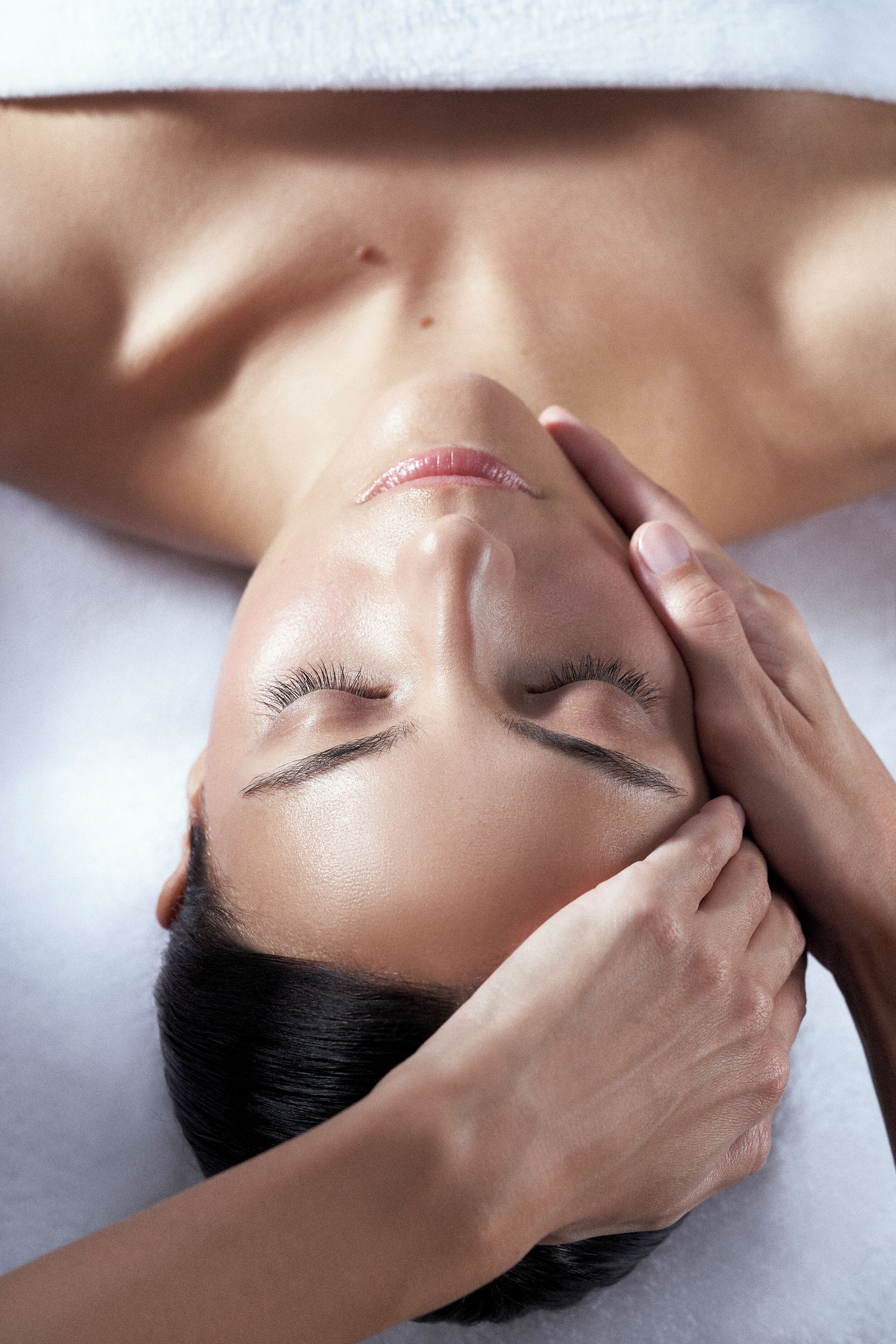 A person lying down with their head resting on a white surface, possibly a bed or massage table.