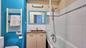 Een badkamer met een blauwe wand, een wit toilet, een wastafel met spiegel erboven en een badkuip met douchekop.