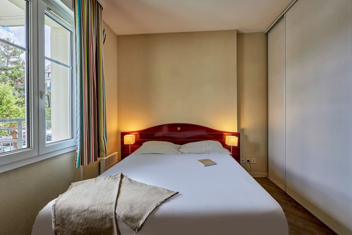Ein Hotelzimmer mit einem großen Bett, zwei Nachttischlampen, einem fenster mit Vorhängen und Blick nach draußen.