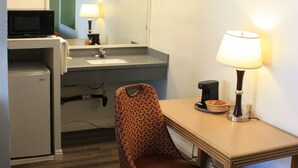 Une chambre d’hôtel équipée d’une kitchenette, d’un bureau avec une lampe, d’une chaise et d’un miroir.