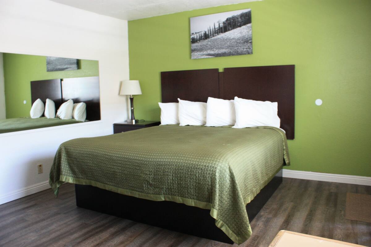 A hotel room with a large bed, green walls, and a framed picture above the bed.