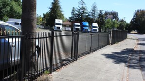 Un espace de stationnement clôturé où se trouvent plusieurs camions et une voiture.