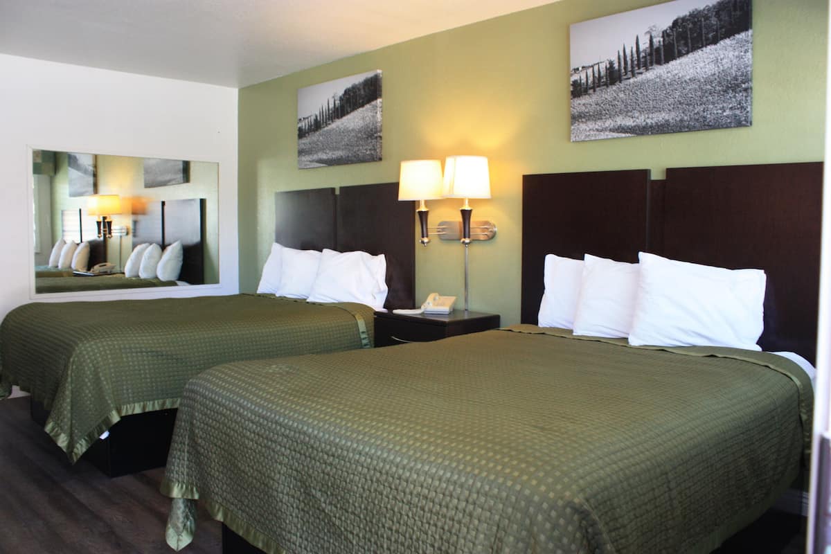A hotel room with two beds, a nightstand with a lamp, and a mirror.